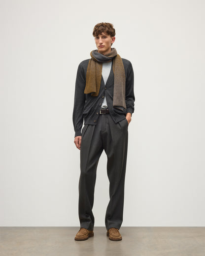 A man modeling a dark charcoal gray suit, featuring a dark gray cardigan, matching trousers, a light gray t-shirt, a brown and gray patterned scarf, and brown suede shoes, standing against a plain light gray studio background.  JOHNSTONS OF ELGIN CASHMERE RIBBED OMBRE PIONEER SCARF GREY 100% CASHMERE HAA03641Q26256ONE