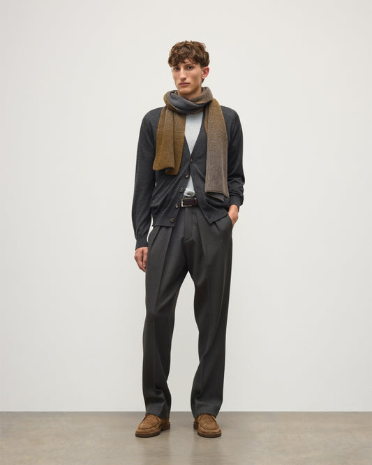 A man modeling a dark charcoal gray suit, featuring a dark gray cardigan, matching trousers, a light gray t-shirt, a brown and gray patterned scarf, and brown suede shoes, standing against a plain light gray studio background.  JOHNSTONS OF ELGIN CASHMERE RIBBED OMBRE PIONEER SCARF GREY 100% CASHMERE HAA03641Q26256ONE