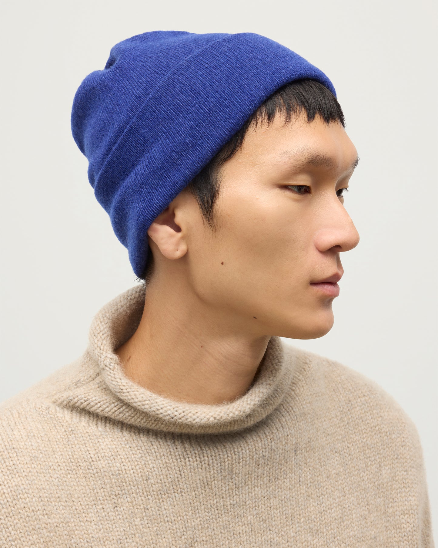 JOHNSTONS OF ELGIN BRAEMAR BEANIE BLUE 100% CASHMERE ON A MALE MODEL WITH NATURAL KESTER CASHMERE FUNNEL NECK SWEATER HAE02655SD5326ONE