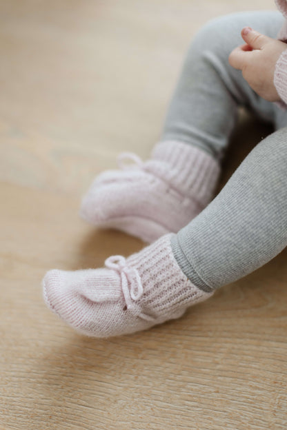 Johnstons of Elgin Hand Knitted Cashmere Baby Booties in Blush on pink check background JA000114SE0208ONE
