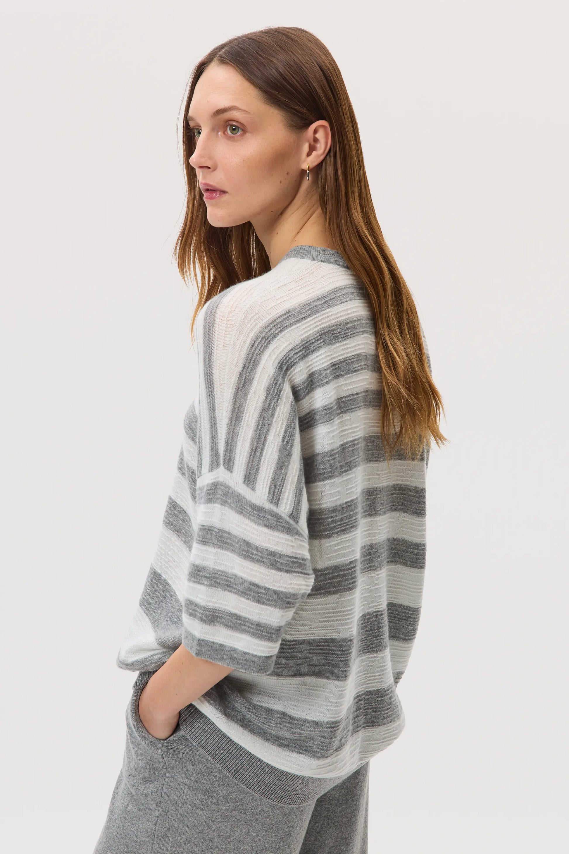Side view of a female model wearing Johnstons of Elgin SS25 Unisex Knitwear Light Grey & White Textured Stripe Oversized Cashmere T-Shirt on a white backdrop KAA05414Q25124