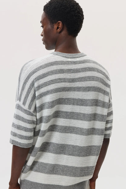 Back view of a male model wearing Johnstons of Elgin SS25 Unisex Knitwear Light Grey & White Textured Stripe Oversized Cashmere T-Shirt on a white backdrop KAA05414Q25124