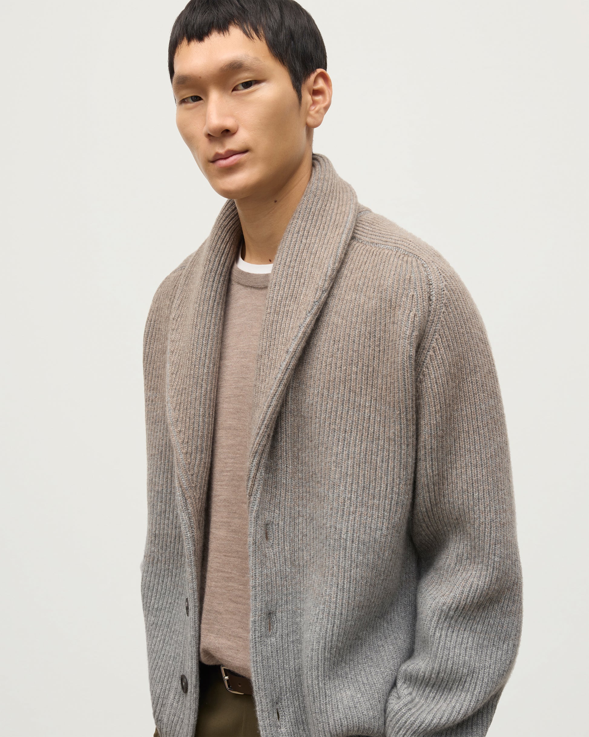 MALE MODEL WEARING JOHNSTONS OF ELGIN PIONEER SHAWL CARDIGAN GREY 100% CASHMERE WITH OLIVE GREEN CHINOS, OVER A SUPERFINE CASHMERE LIGHT BROWN SWEATER AND WHITE T-SHIRT KAA05750Q25948
