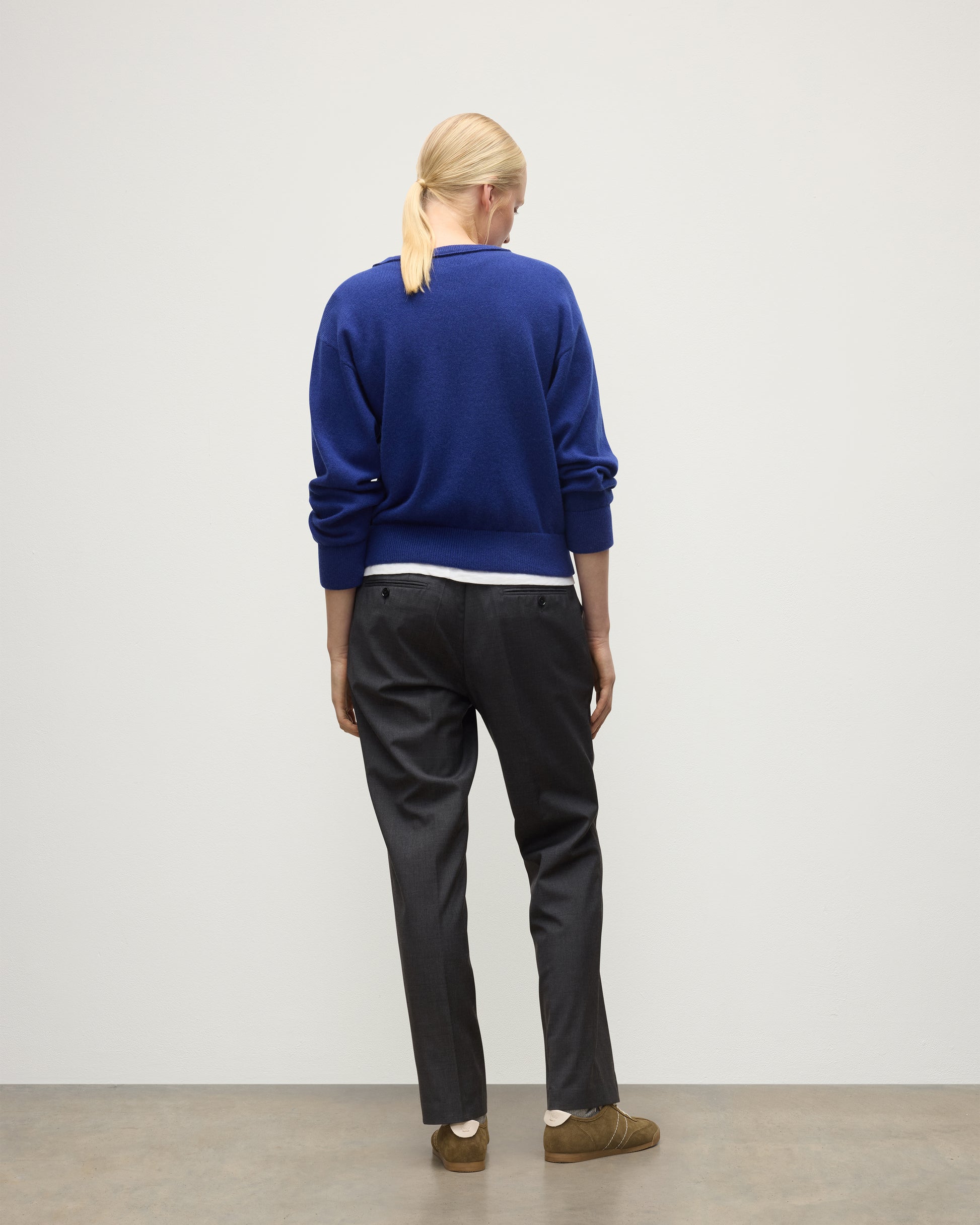 BACK OF MODEL WEARING JOHNSTONS OF ELGIN WOMENS STELLA SWEATSHIRT BLUE 100% CASHMERE OVER A WHITE T_SHIRT, WITH DARK GREY TROUSERS KAA05770SD5326