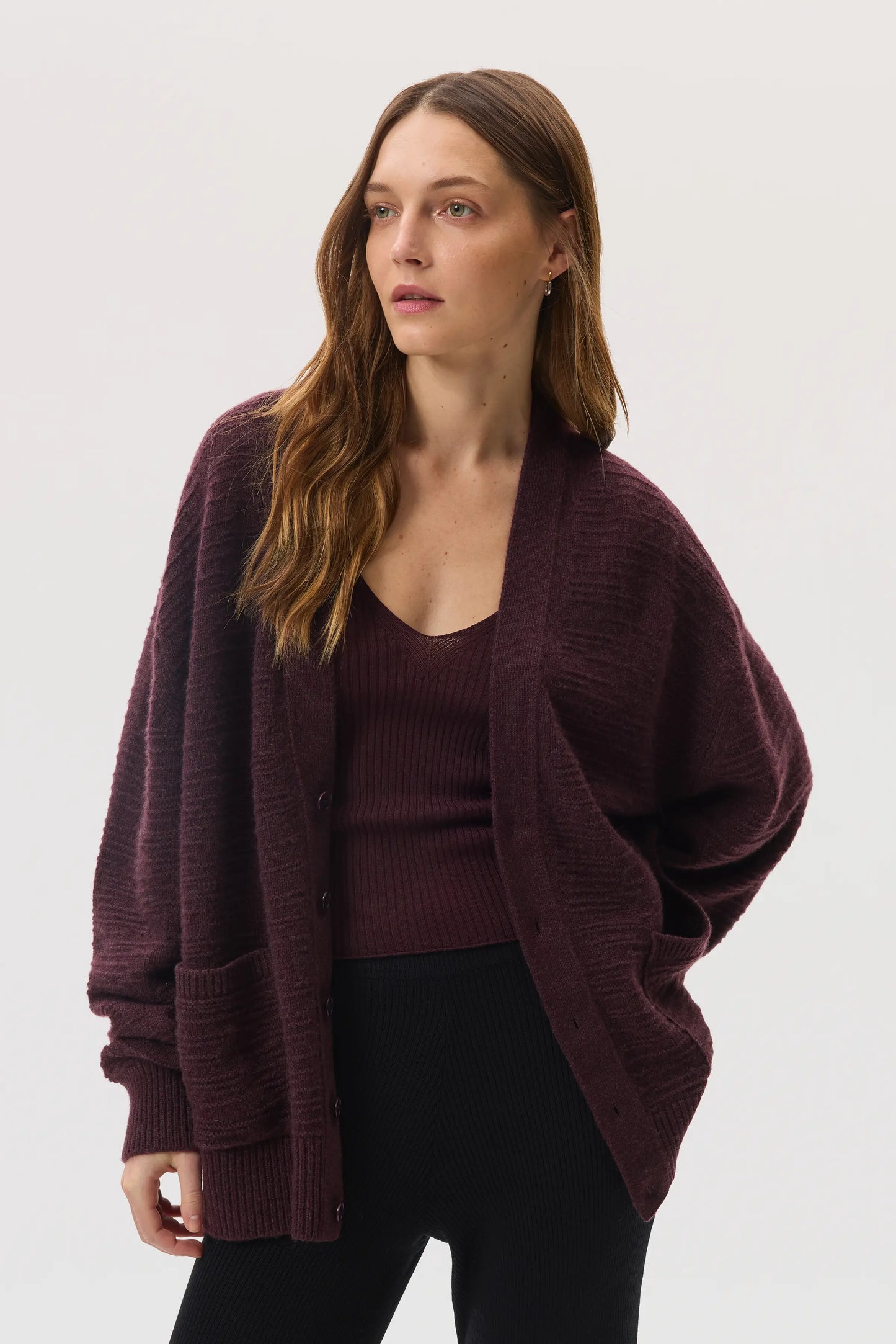 Female model wearing Johnstons of Elgin SS25 Unisex Knitwear Rosewood Textured Cashmere Cardigan with superfine cashmere vest, black trousers KAC05415SB7089