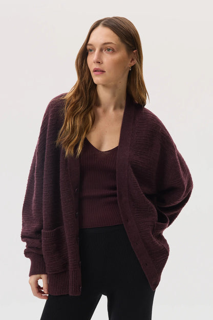 Female model wearing Johnstons of Elgin SS25 Unisex Knitwear Rosewood Textured Cashmere Cardigan with superfine cashmere vest, black trousers KAC05415SB7089