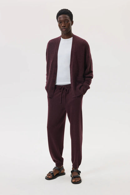 Male model wearing Johnstons of Elgin SS25 Unisex Knitwear Rosewood Textured Cashmere Cardigan with superfine cashmere sweater in white, and rosewood cashmere jogger against a white background KAC05415SB7089