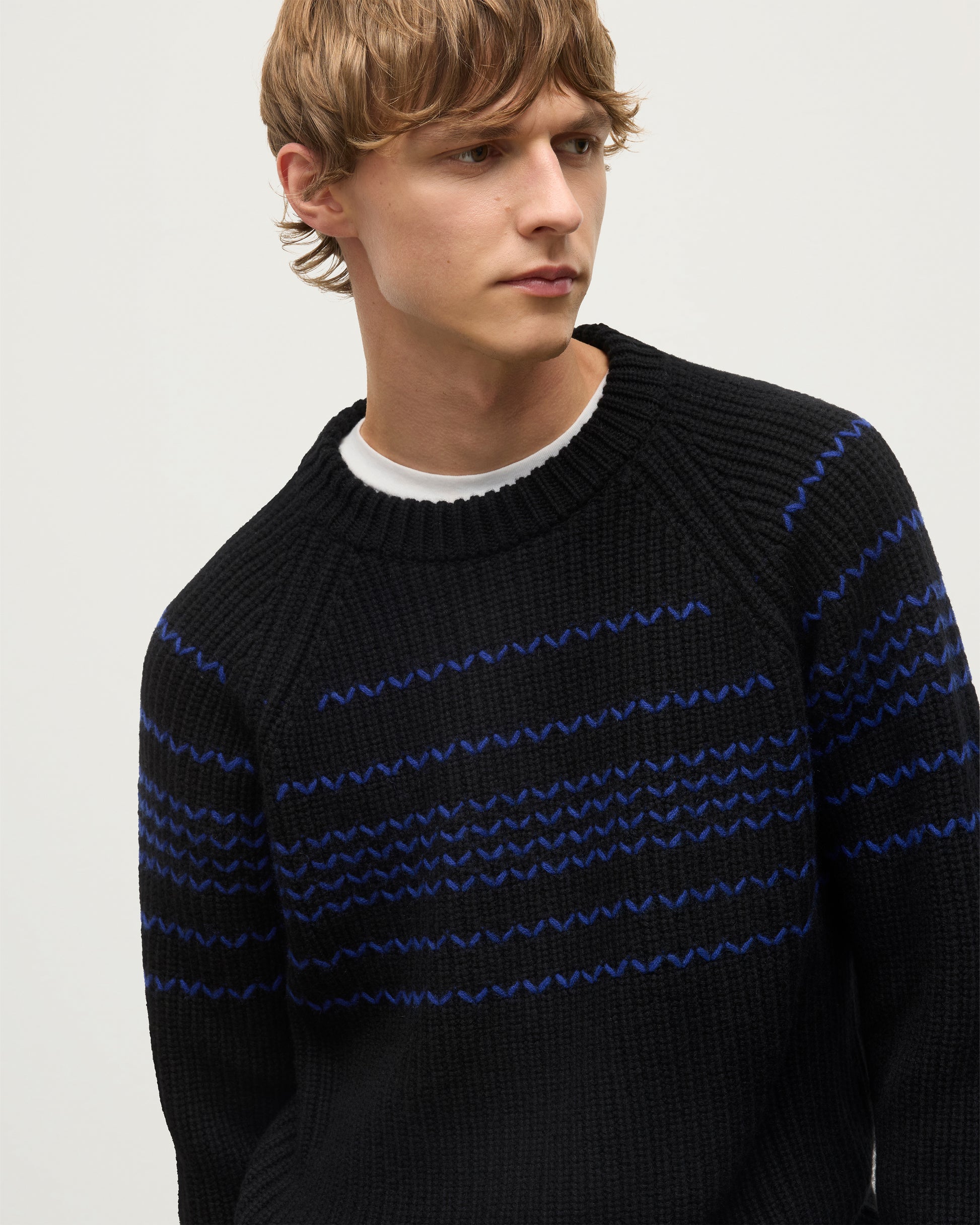MODEL WEARS JOHNSTONS OF ELGIN  MENS SUMMIT CREW SWEATER BLACK & BLUE 100% CASHMERE OVER A WHITE T-SHIRT WITH NAVY TROUSERS KAC05752Q25949