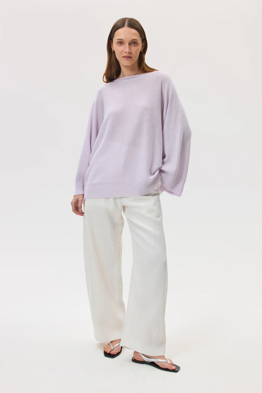 Model wears Johnstons of Elgin SS25 Women's Knitwear Lavender Cashmere Cape Jumper with white trousers KAI05048HD0086