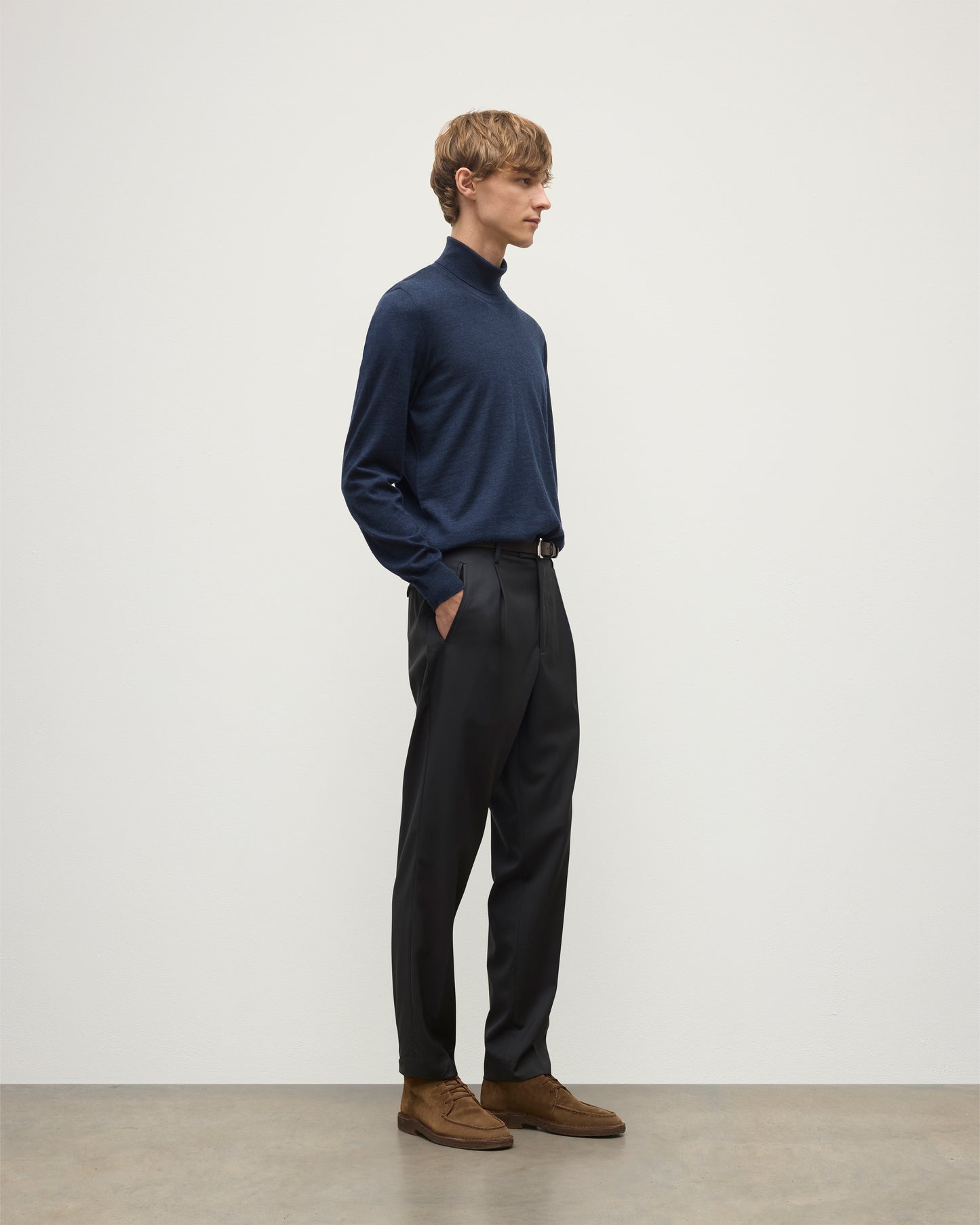 MODEL WEARS JOHNSTONS OF ELGIN MENS SUPERFINE FIN ROLL COLLAR NAVY 100% SUPERFINE CASHMERE  WITH GREY TROUSERS AND BROWN BELT KAI05333HD7350