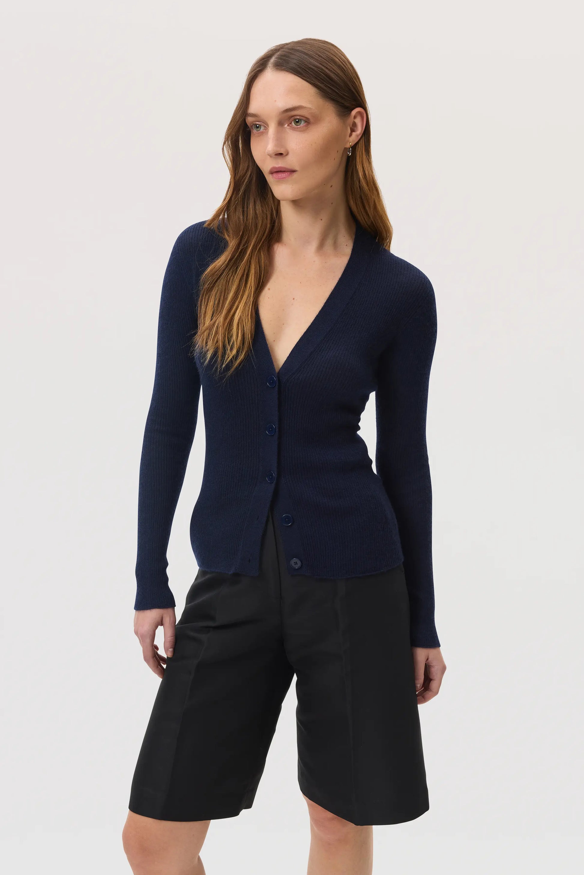 Model wearing Johnstons of Elgin SS25 Women's Knitwear Navy Superfine Cashmere Ribbed Cardigan with black shorts KAI05372SD7600