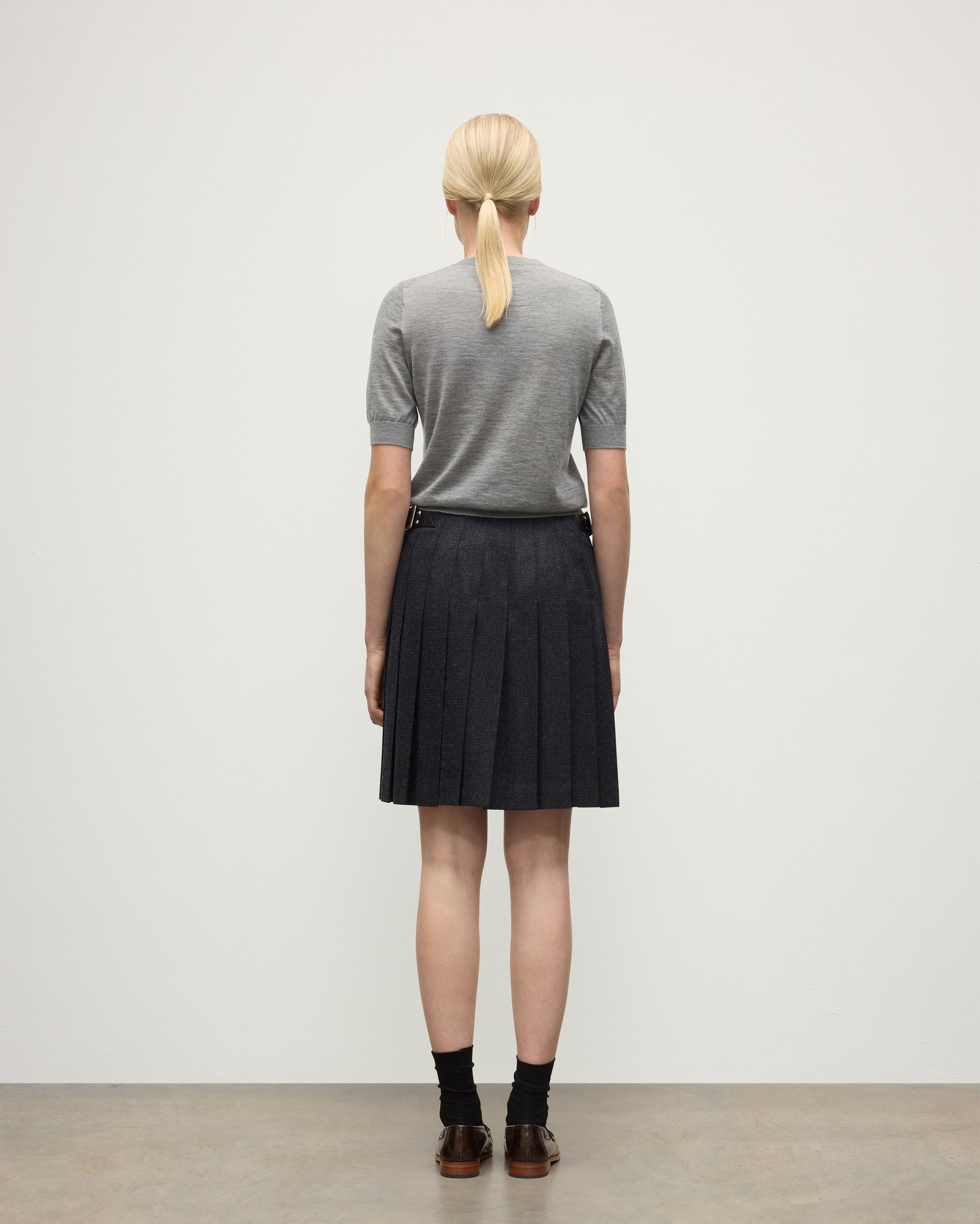 BACK VIEW OF A MODEL WEARING JOHNSTONS OF ELGIN WOMENS HONOR SHORT SLEEVE CREW GREY 100% SUPERFINE CASHMERE WITH SHORT LE KILT CHARCOAL KILT  KAI05712HA4253