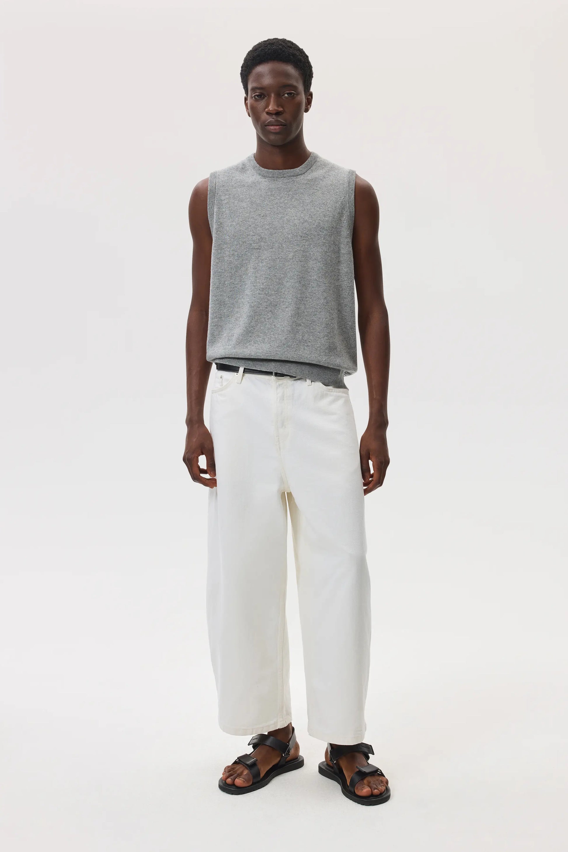 Male model wearing Johnstons of Elgin SS25 Unisex Knitwear Light Grey Cashmere Tank and white trousers against a white background  KAP05243HA0308