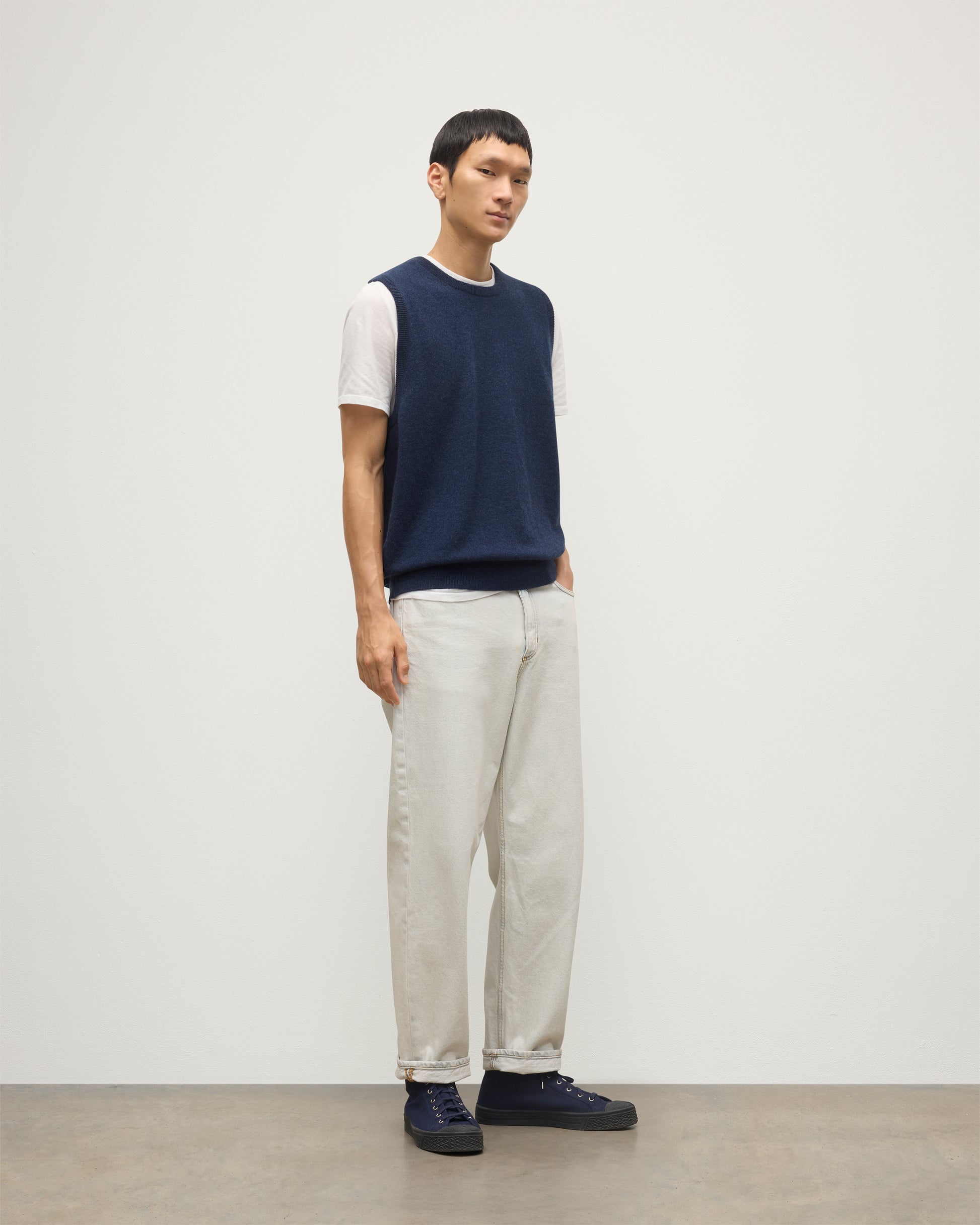 MODEL WEARS JOHNSTONS OF ELGIN MENS LENNOX SLEEVELESS CREW NAVY 100% CASHMERE, OVER A WHITE SHORT SLEEVE T-SHIRT WITH WHITE JEANS KAP05243HD7350
