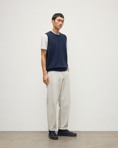 MODEL WEARS JOHNSTONS OF ELGIN MENS LENNOX SLEEVELESS CREW NAVY 100% CASHMERE, OVER A WHITE SHORT SLEEVE T-SHIRT WITH WHITE JEANS KAP05243HD7350