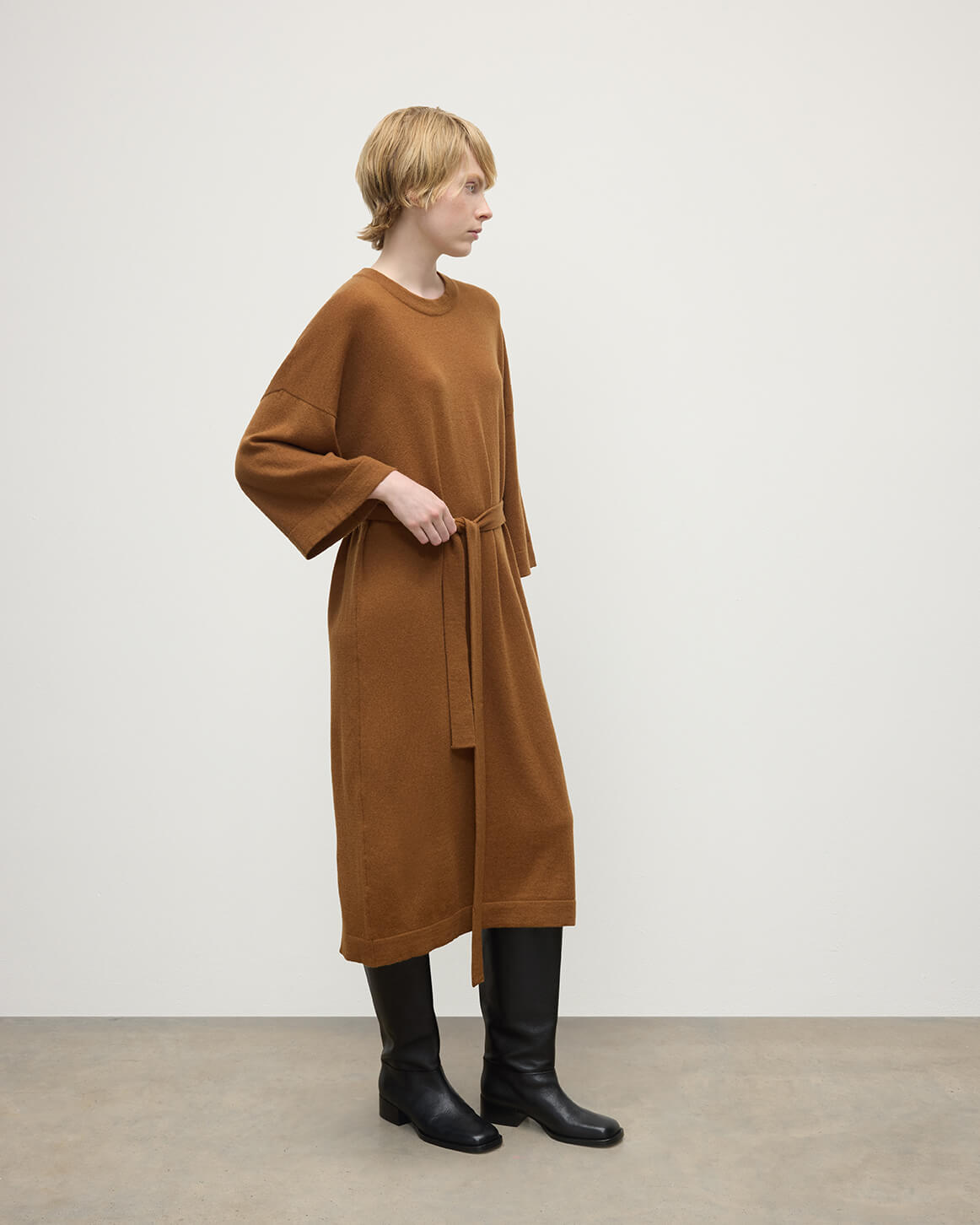 Model wears Johnstons of Elgin AW25 Women's Knitwear Dark Camel Tie-Waist Cashmere Camel Jumper Dress Side View  KAP05490SB4620