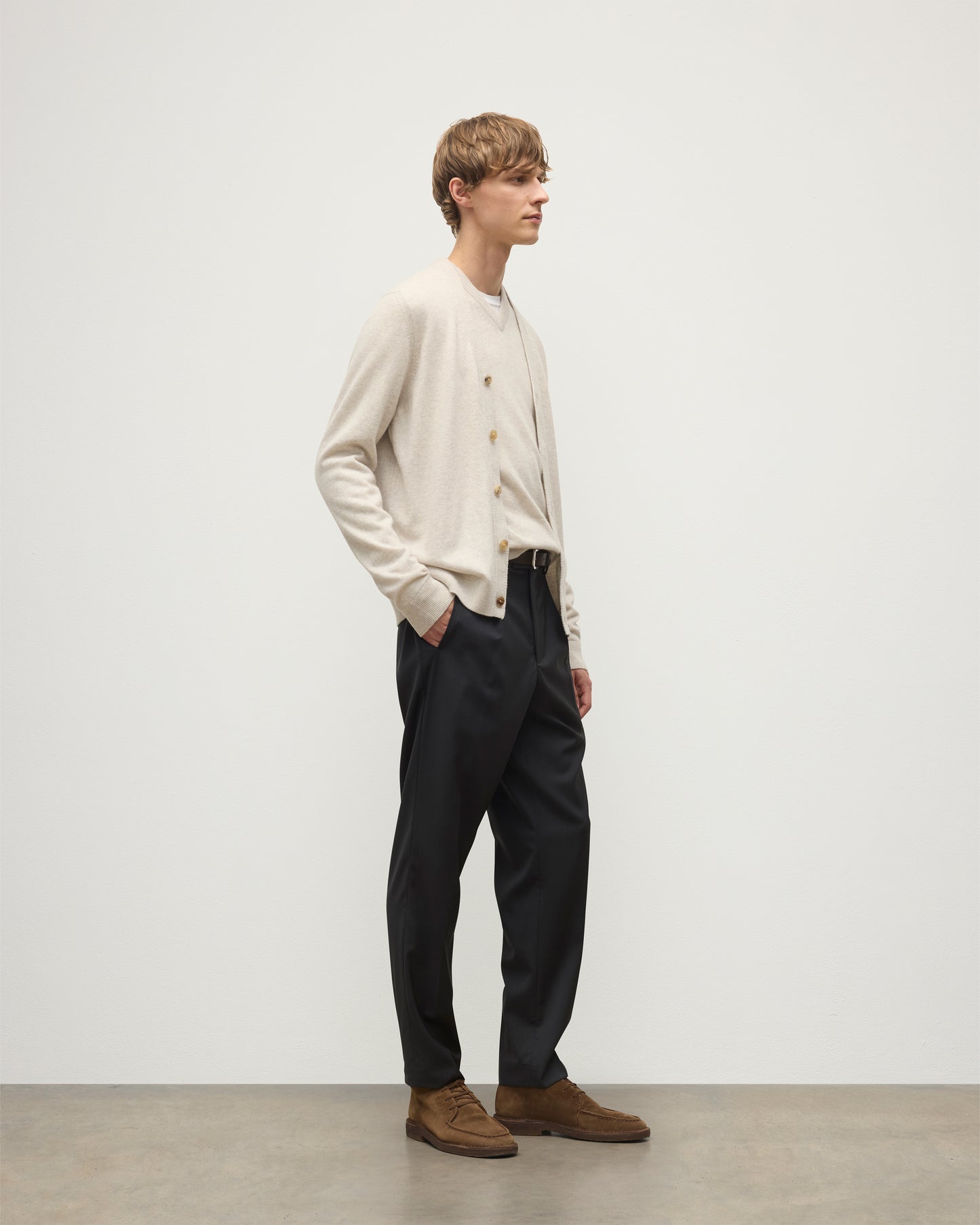 MODEL WEARS JOHNSTONS OF ELGIN MENS RORY VEE NECK CLASSIC CARDIGAN NATURAL 100% CASHMERE OVER A MATCHING V NECK SWEATER WITH GREY TROIUSERS KAP05576HA0402