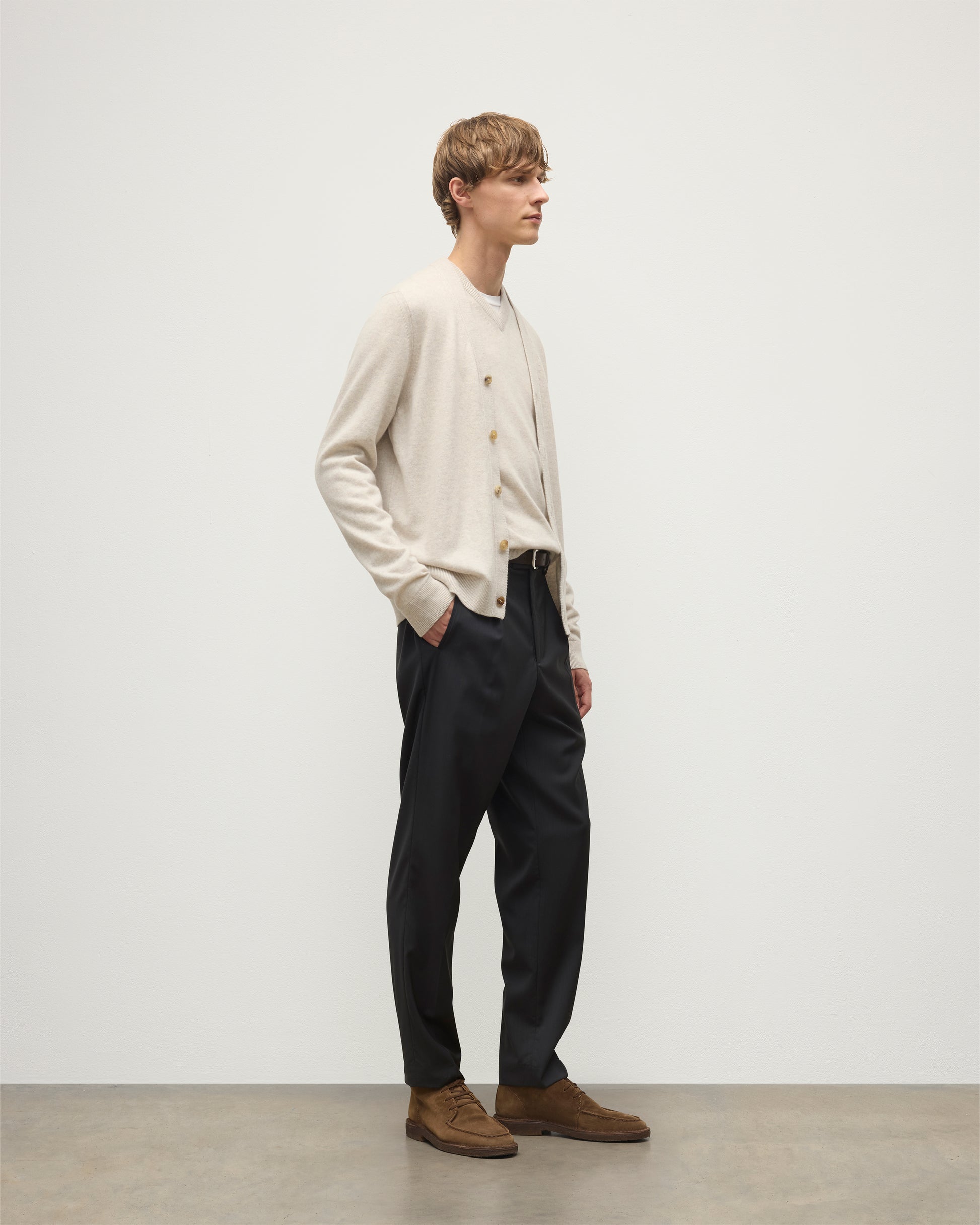 MODEL WEARS JOHNSTONS OF ELGIN MENS RORY VEE NECK CLASSIC CARDIGAN NATURAL 100% CASHMERE OVER A MATCHING V NECK SWEATER WITH GREY TROIUSERS KAP05576HA0402