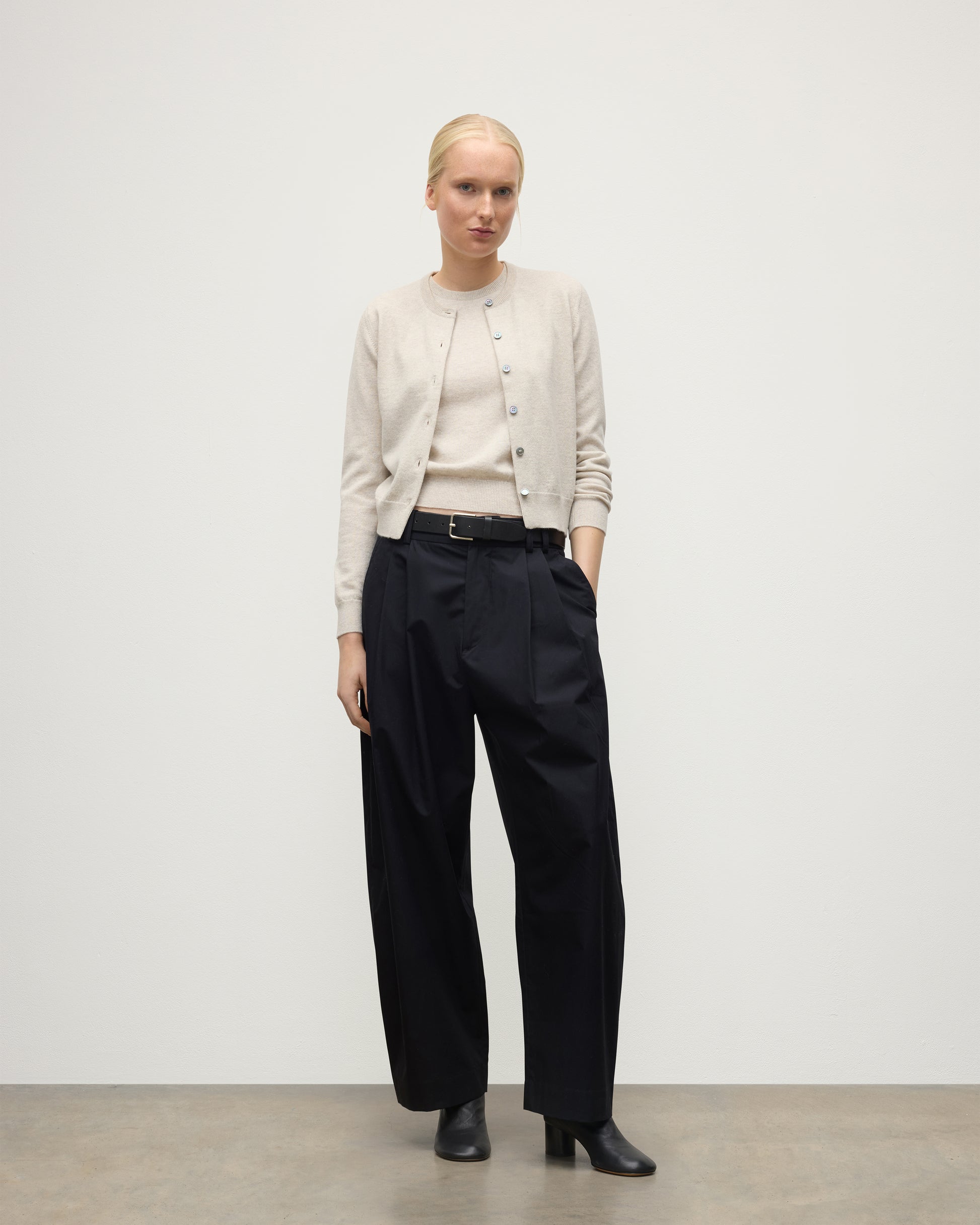 MODEL WEARING JOHNSTONS OF ELGIN WOMENS IRIS CLASSIC CREW CARDIGAN NATURAL 100% CASHMERE WITH NAVY TROUSERS AND BLACK BOOTS KAP05704HA0402