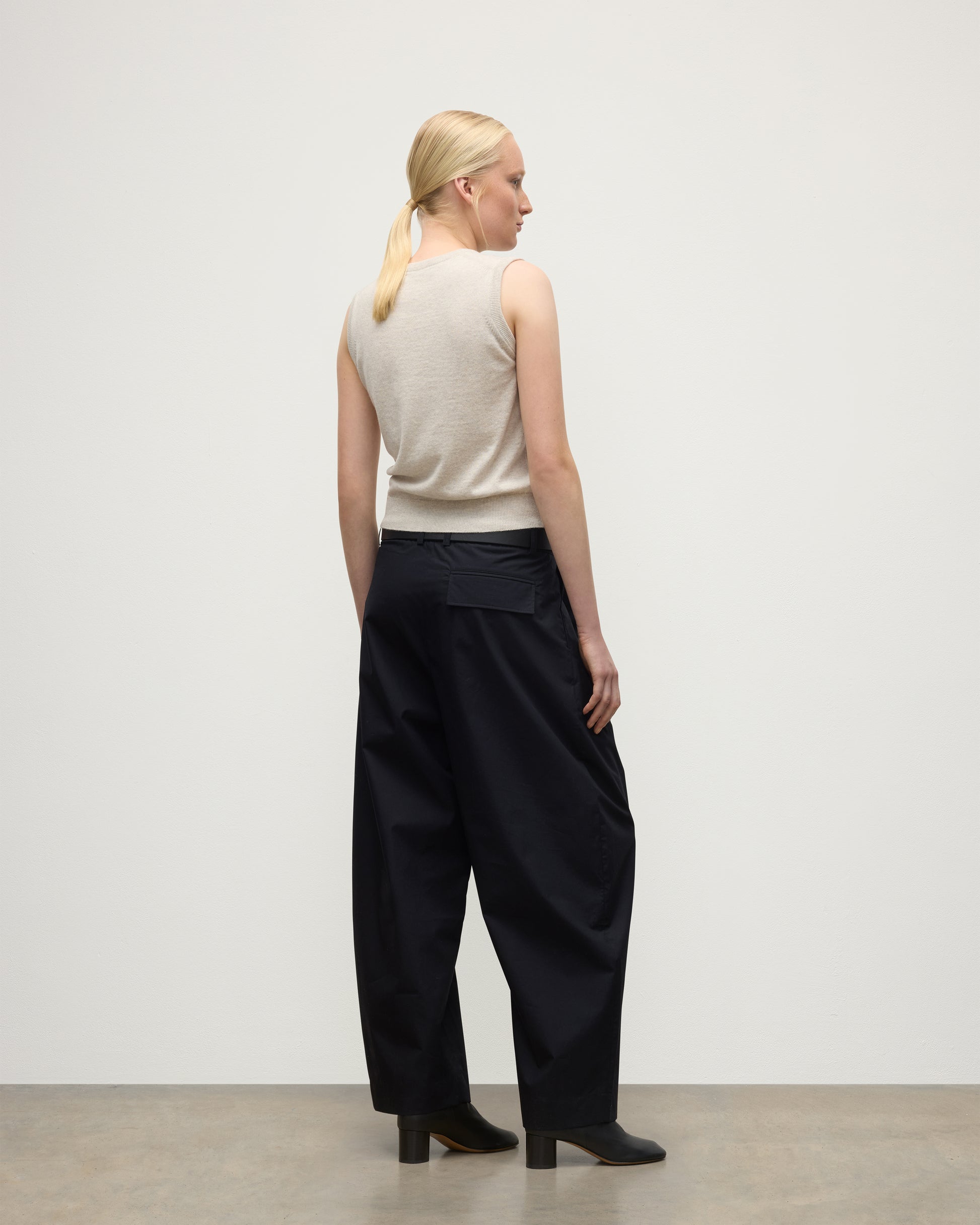 MODEL WEARS JOHNSTONS OF ELGIN WOMENS IRIS CLASSIC SLEEVELESS CREW NATURAL 100% CASHMERE WITH NAVY TROUSERS AND BLACK BOOTS  KAP05705HA0402