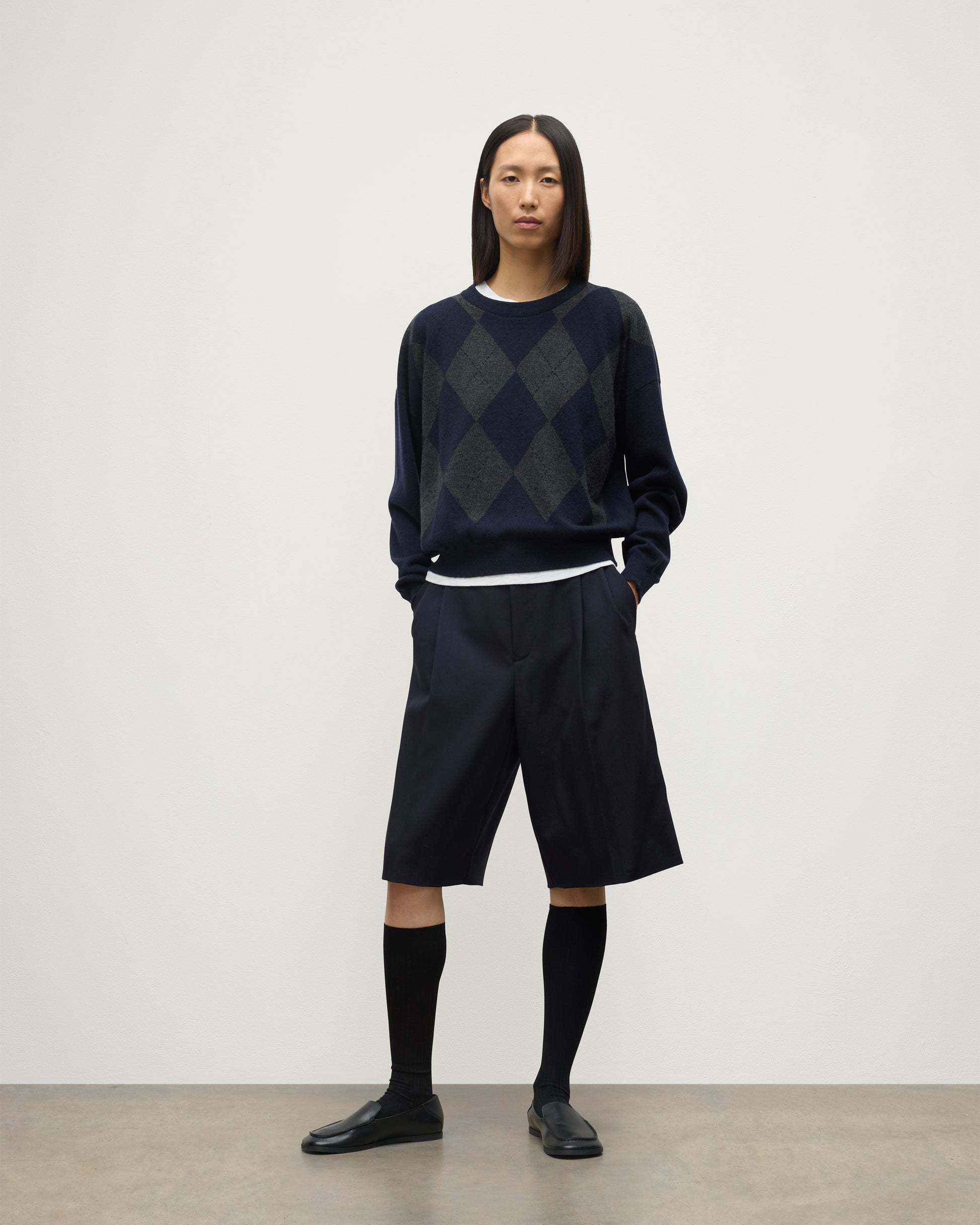 MODEL WEARS JOHNSTONS OF ELGIN WOMENS CLAN SLOUCH CREW NAVY 100% CASHMERE OVER A WHITE TEE, WITH NAVY LONG SHORTS, CASHMERE SOCKS AND LOAFERS KAP05732JU1606