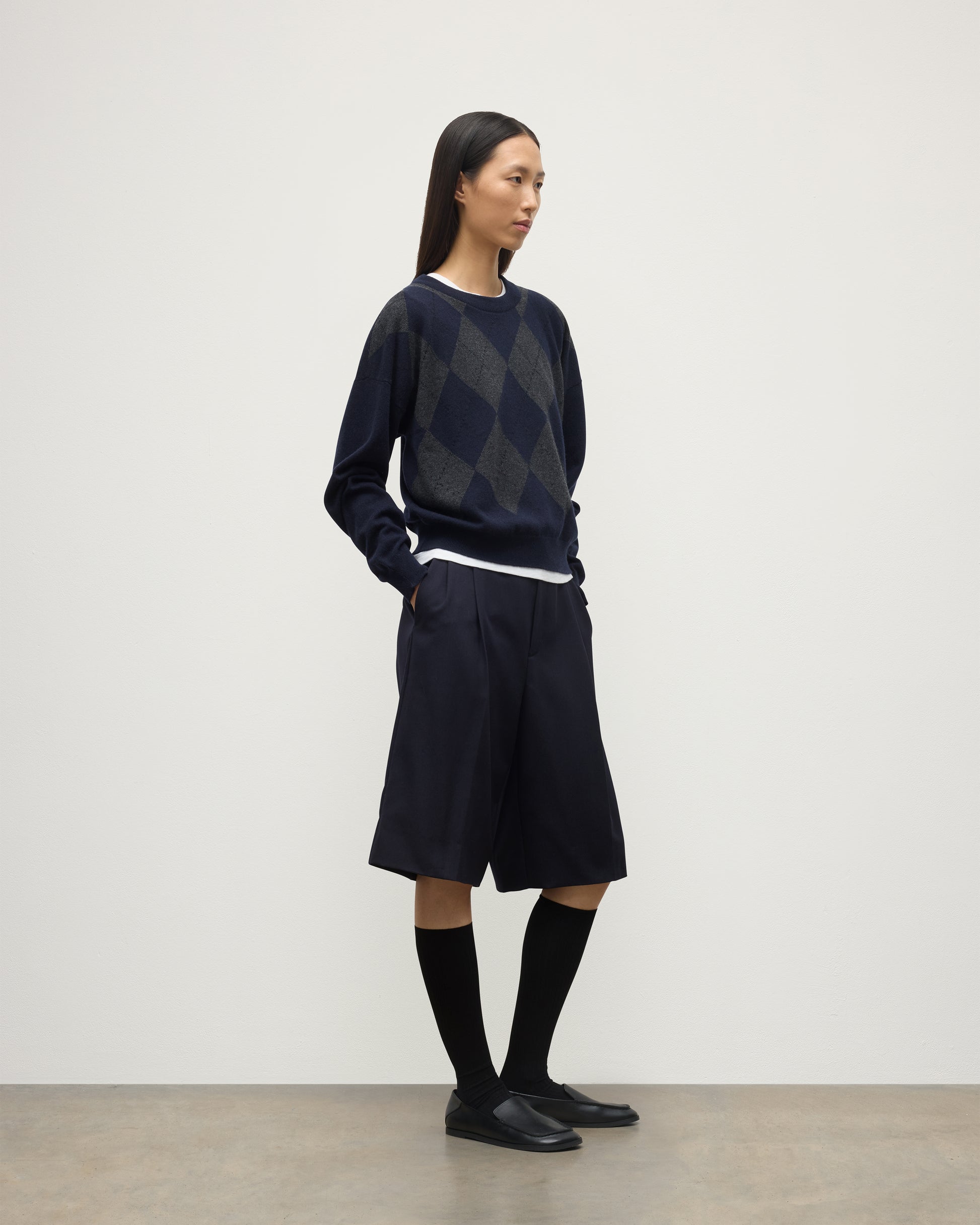 MODEL WEARS JOHNSTONS OF ELGIN WOMENS CLAN SLOUCH CREW NAVY 100% CASHMERE OVER A WHITE TEE, WITH NAVY LONG SHORTS, CASHMERE SOCKS AND LOAFERS KAP05732JU1606