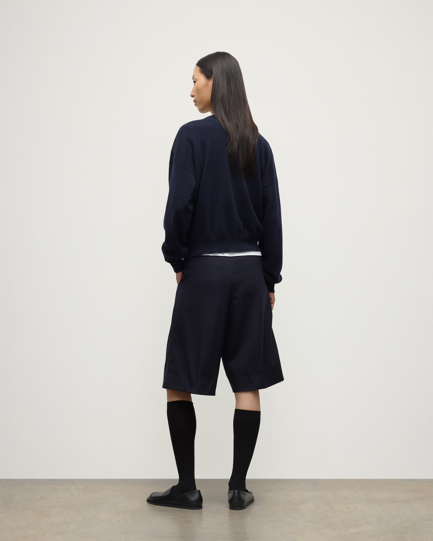 MODEL WEARS JOHNSTONS OF ELGIN WOMENS CLAN SLOUCH CREW NAVY 100% CASHMERE OVER A WHITE TEE, WITH NAVY LONG SHORTS, CASHMERE SOCKS AND LOAFERS KAP05732JU1606