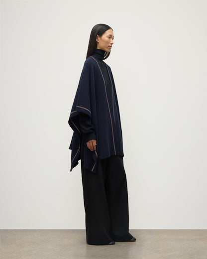 MODEL WEARS JOHNSTONS OF ELGIN WOMENS HAWK PONCHO NAVY 100% CASHMERE OVER NAVY ROLL NECK SWEATER AND NAVY TROUSERS KAU05769Q25973O/S