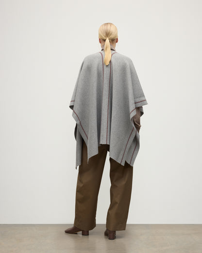 MODEL WEARS JOHNSTONS OF ELGIN WOMENS HAWK PONCHO LIGHT GREY 100% CASHMERE OVER A NATURAL CASHMERE SWEATER AND BROWN TROUSERS KAU05769Q25974O/S