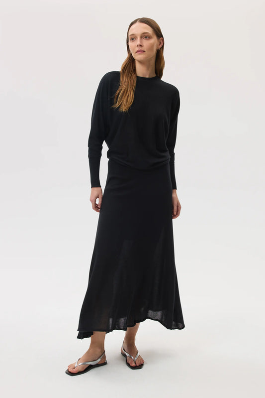 Model wears Johnstons of Elgin SS25 Women's Knitwear Black Cashmere Silk Batwing Jumper with matching black skirt on a white backdrop KBI00975SA0900