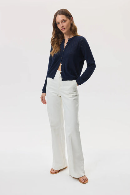 Model wears Johnstons of Elgin SS25 Women's Knitwear Navy Superfine Merino Pointelle Argyle Cardigan with white trousers and sandals KDI00742SD7563